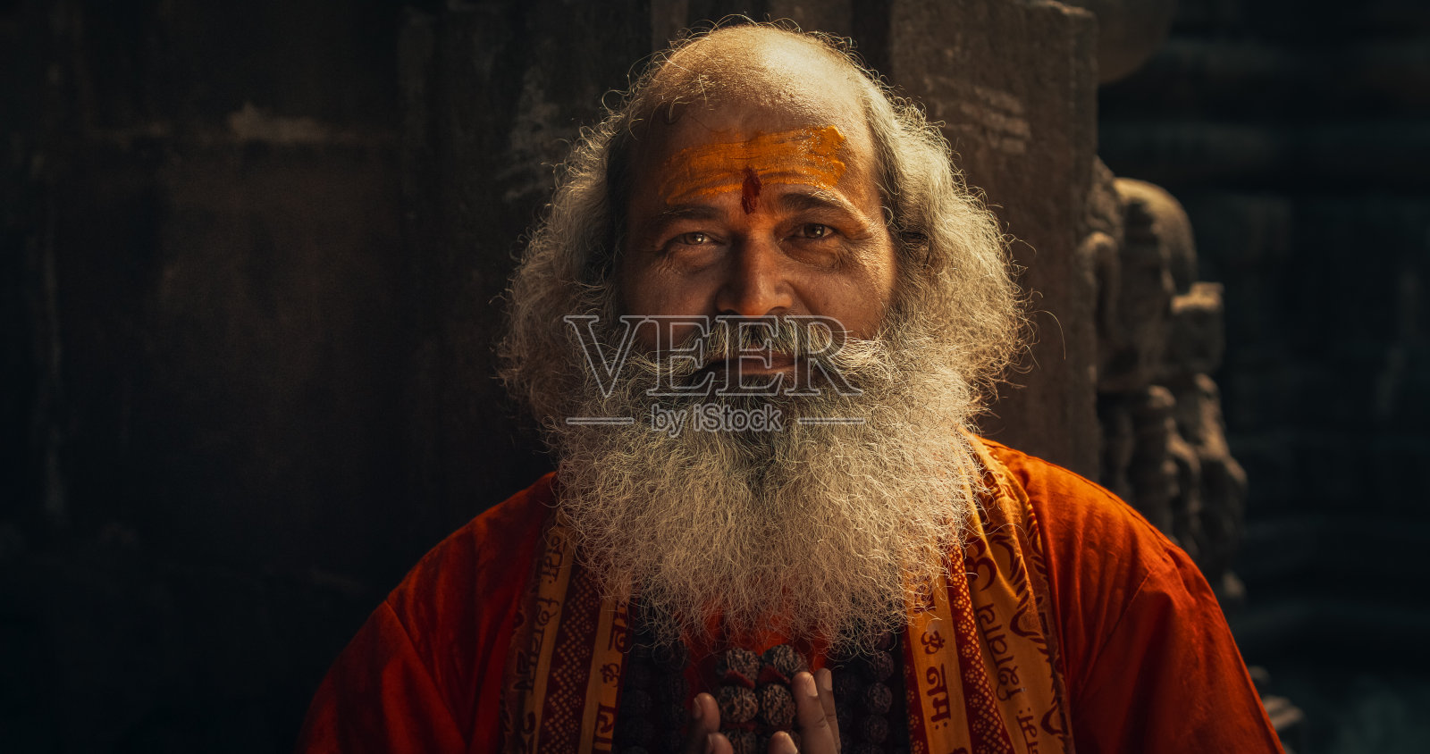 在一座古老的寺庙里，一位年长的印度和尚对着镜头微笑的肖像。友好的印度老人假装从他的宗教中寻求指导和智慧照片摄影图片