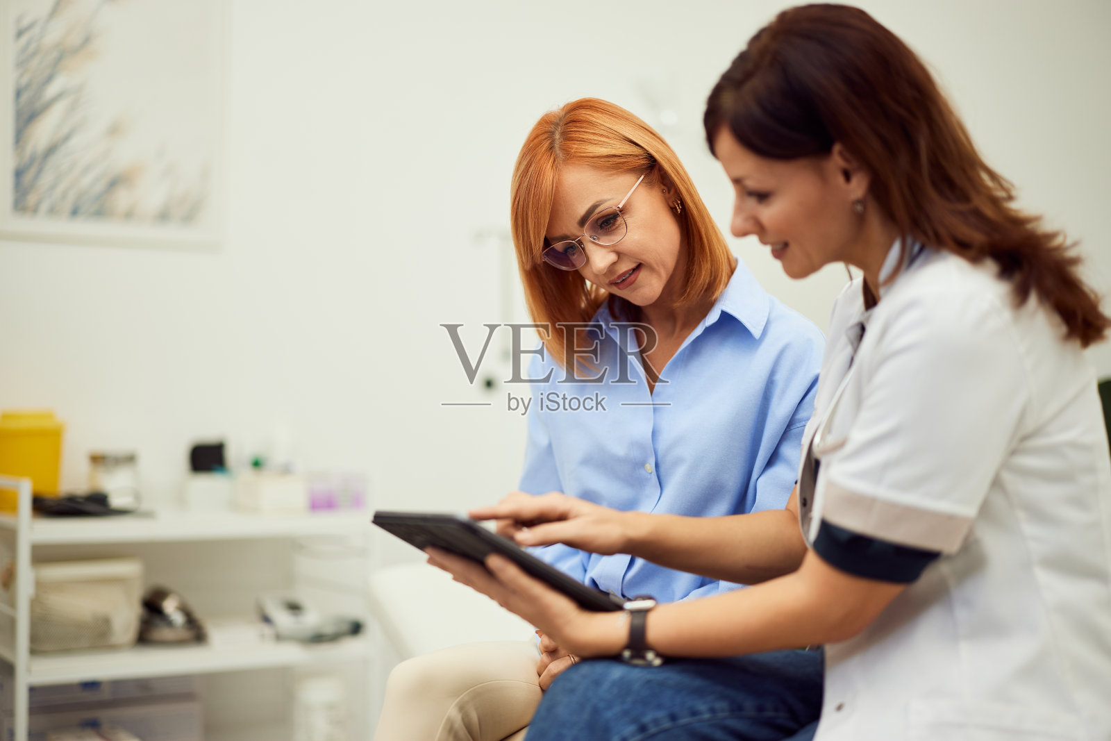 一位女医生在医生的办公室里给姜黄色头发的女病人看检查结果。照片摄影图片