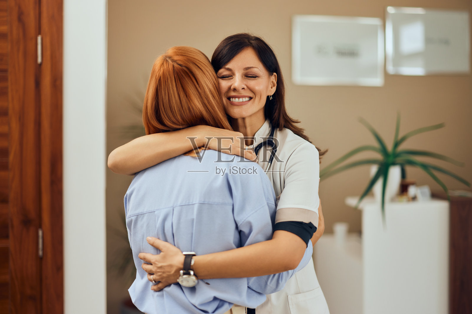 一位黑头发的女医生微笑着拥抱着一位女病人，站在医生的办公室里。照片摄影图片
