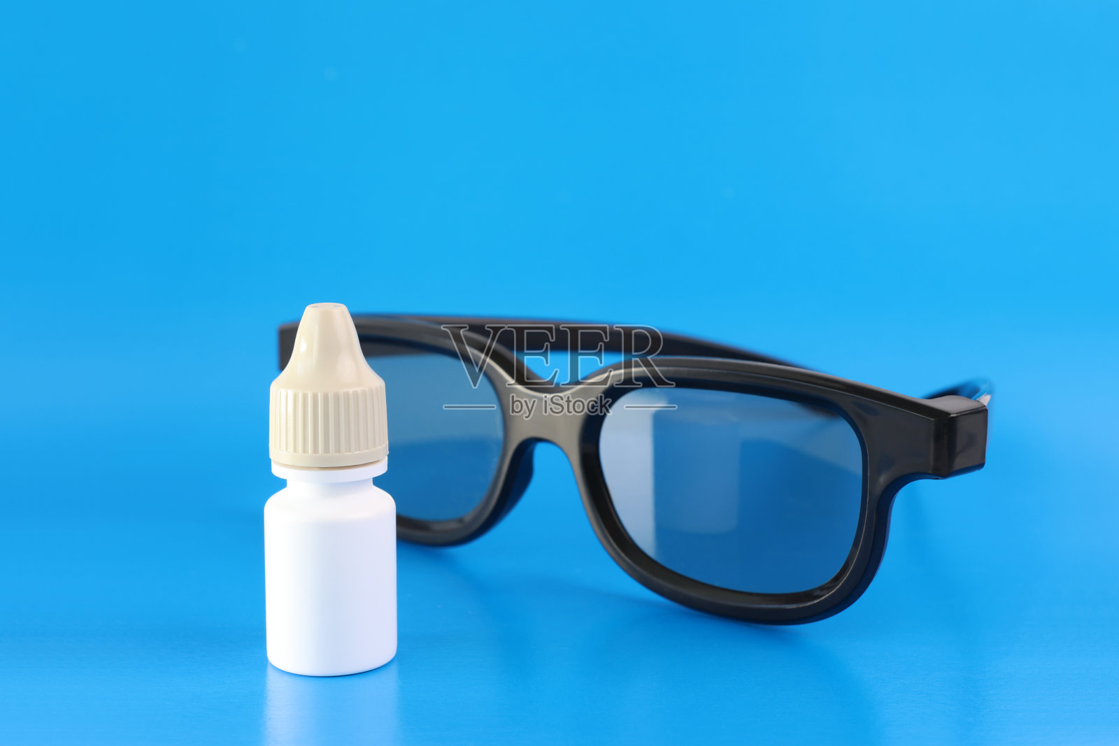 一瓶眼药水和蓝色背景的眼镜。照片摄影图片