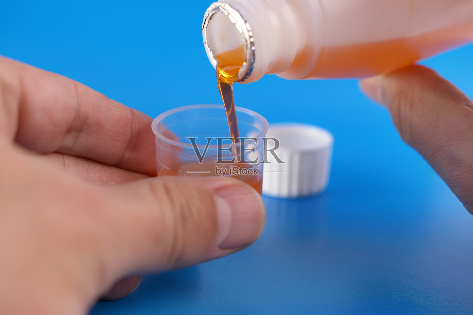 将药用糖浆倒入一个容器中，容器中有蓝色背景上的液体体积划分。治疗和预防疾病。加强免疫力。照片摄影图片
