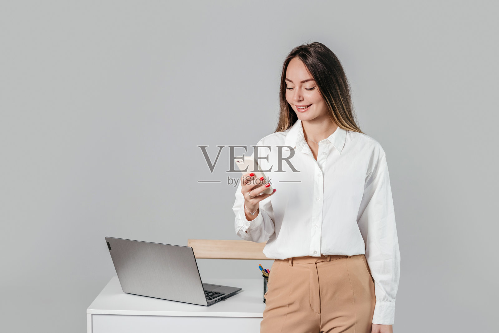 一个微笑着拿着手机的女商人被孤立在灰色的背景中照片摄影图片