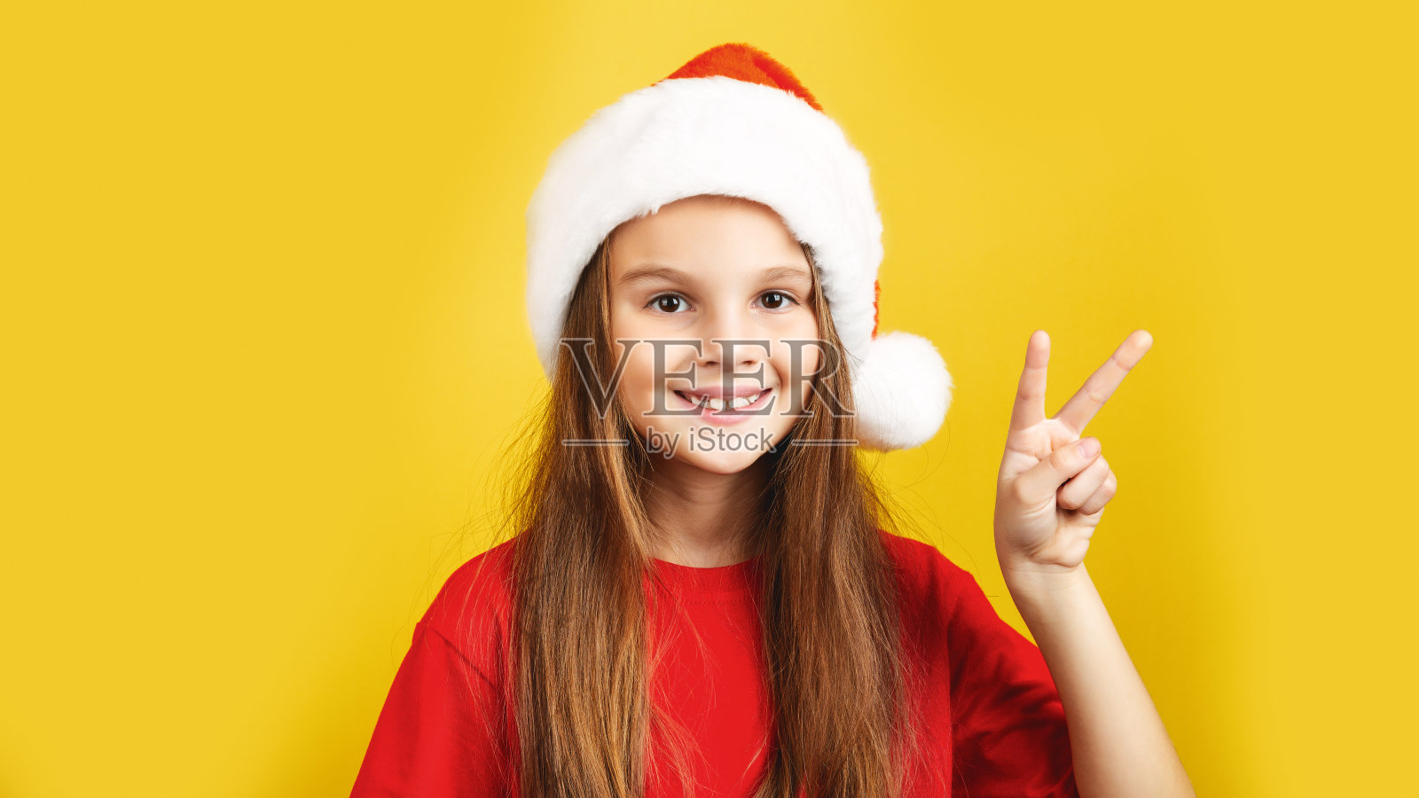 孩子戴着红色的圣诞老人帽，小女孩的肖像微笑着。节日圣诞或新年的概念，工作室拍摄孤立的黄色背景照片摄影图片