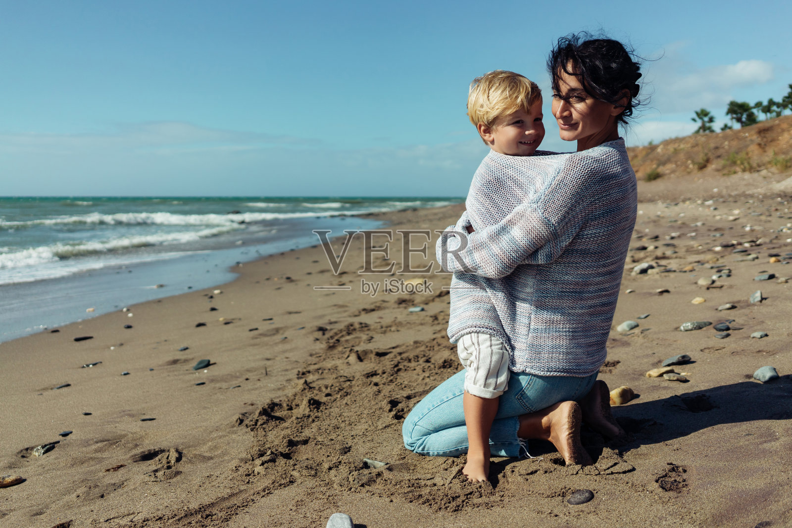 妈妈在海边拥抱她三岁的儿子。照片摄影图片