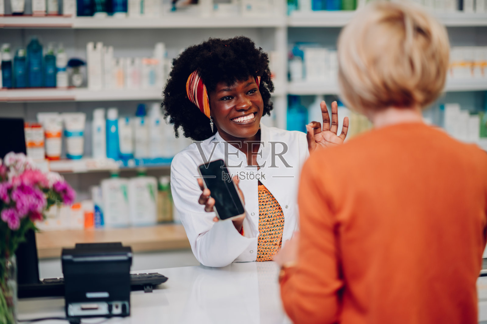 黑人女药剂师在药房用智能手机和老顾客聊天照片摄影图片