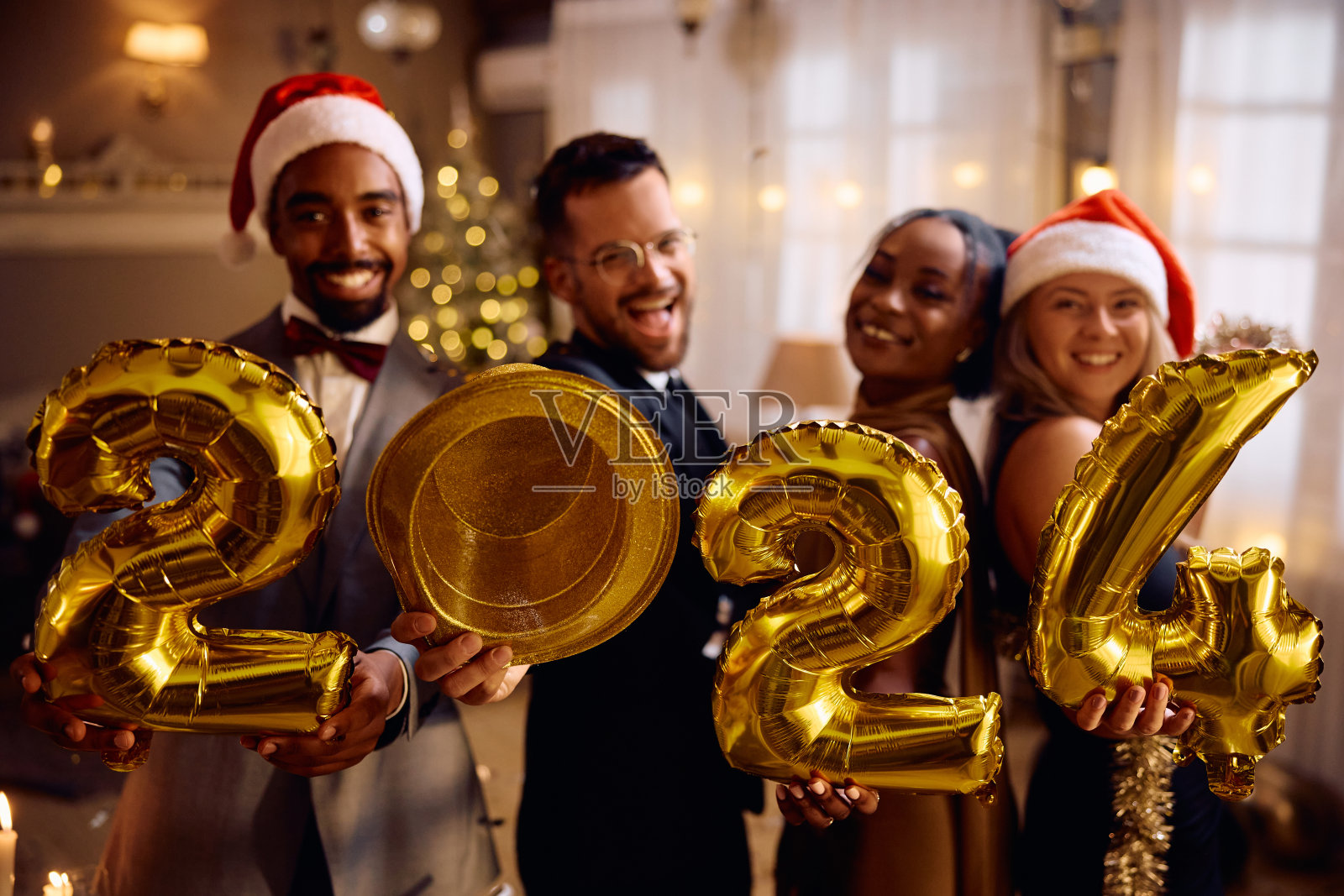快乐的多种族朋友带着2024个金色气球在新年聚会上看着镜头。照片摄影图片
