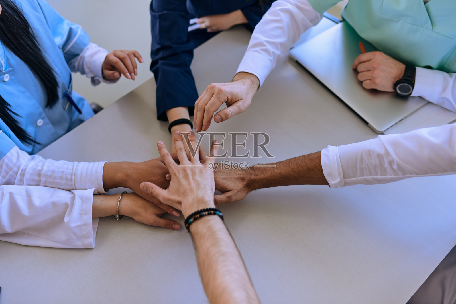 一群医生和一名护士把手放在桌子上，展示了他们在医疗领域坚定不移的团队精神和团结精神照片摄影图片