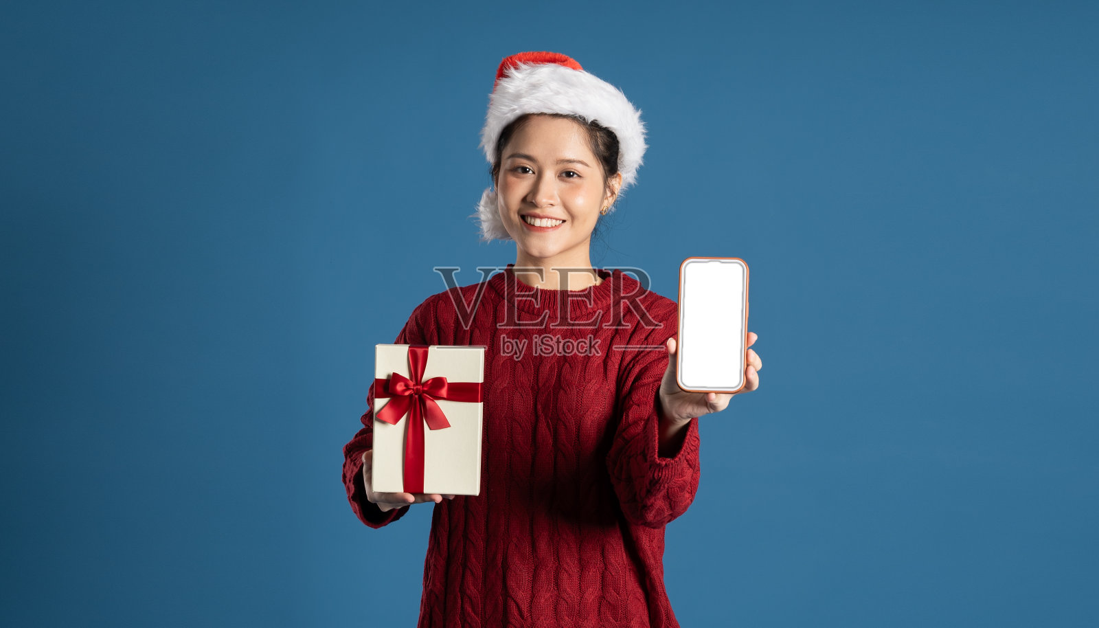 美丽的女人戴着圣诞老人的帽子，孤立在蓝色的墙上照片摄影图片