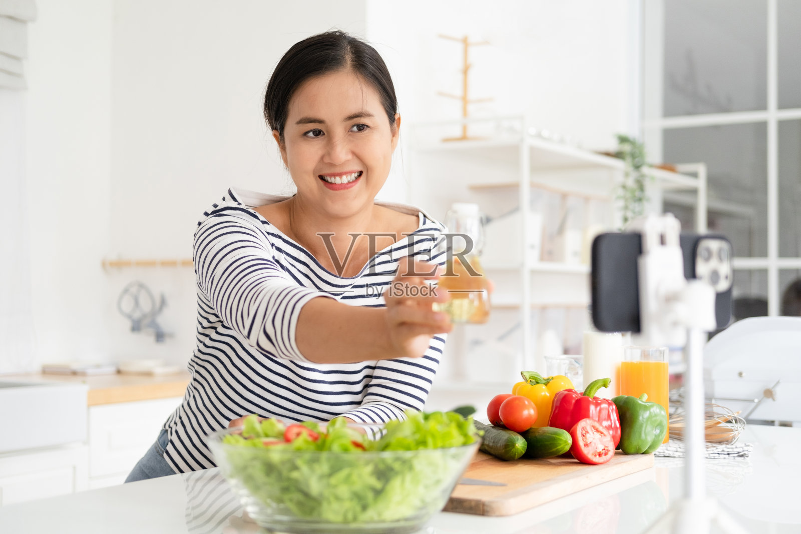 视频博主年轻女性博主和影响者展示吃健康食品沙拉的健康保健。女子用智能手机在线直播卖食品代替贴身减肥。照片摄影图片