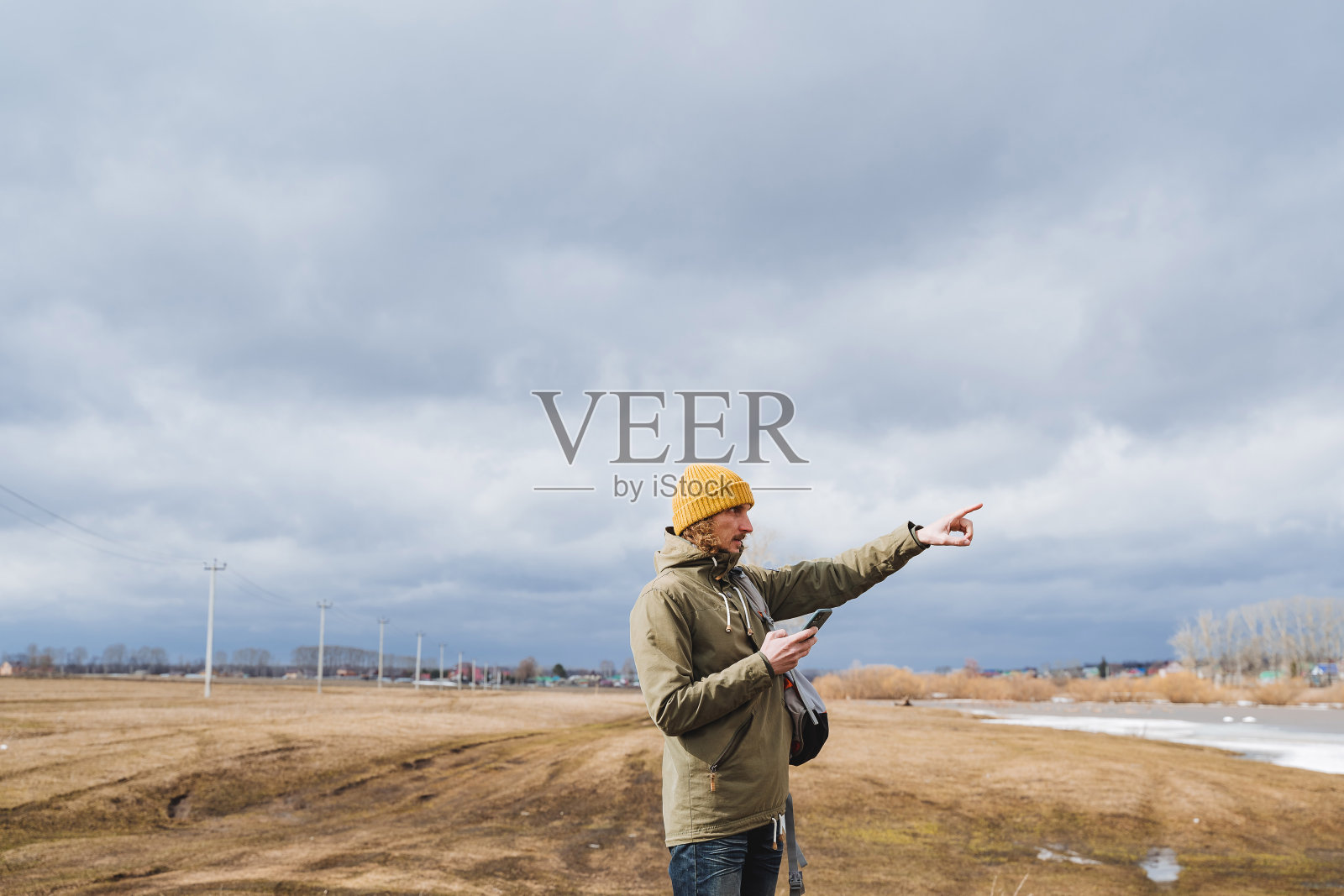 一个徒步旅行的男游客在地面上用手指指示自己的方向，一个潮人拿着手机照片摄影图片