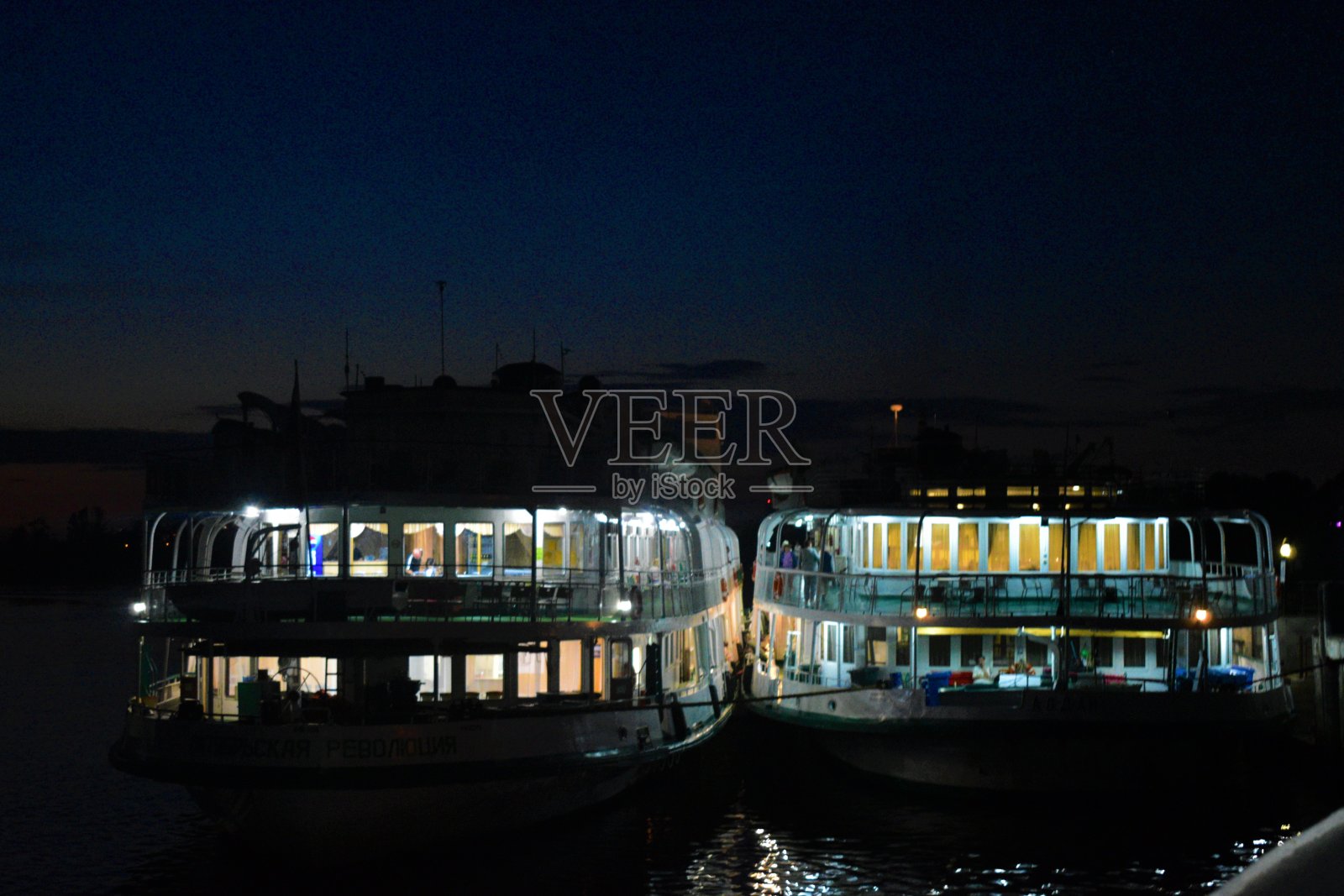 夜里，两艘汽船停在港口，里面有电灯照亮。照片摄影图片