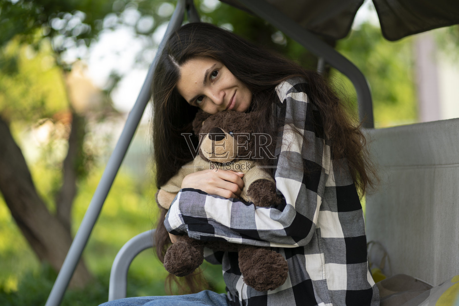 可爱的微笑的女性在户外抱着一个泰迪熊玩具，表现出一些爱照片摄影图片