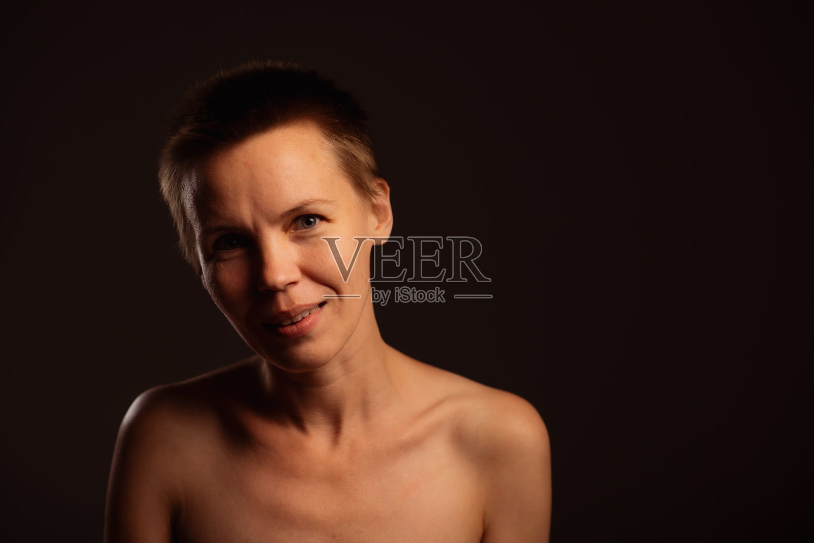 这张照片是在黑色背景下拍摄的，描绘了一位短发、露肩的中年妇女。她迷人的脸上散发出一种俏皮而诱人的表情照片摄影图片