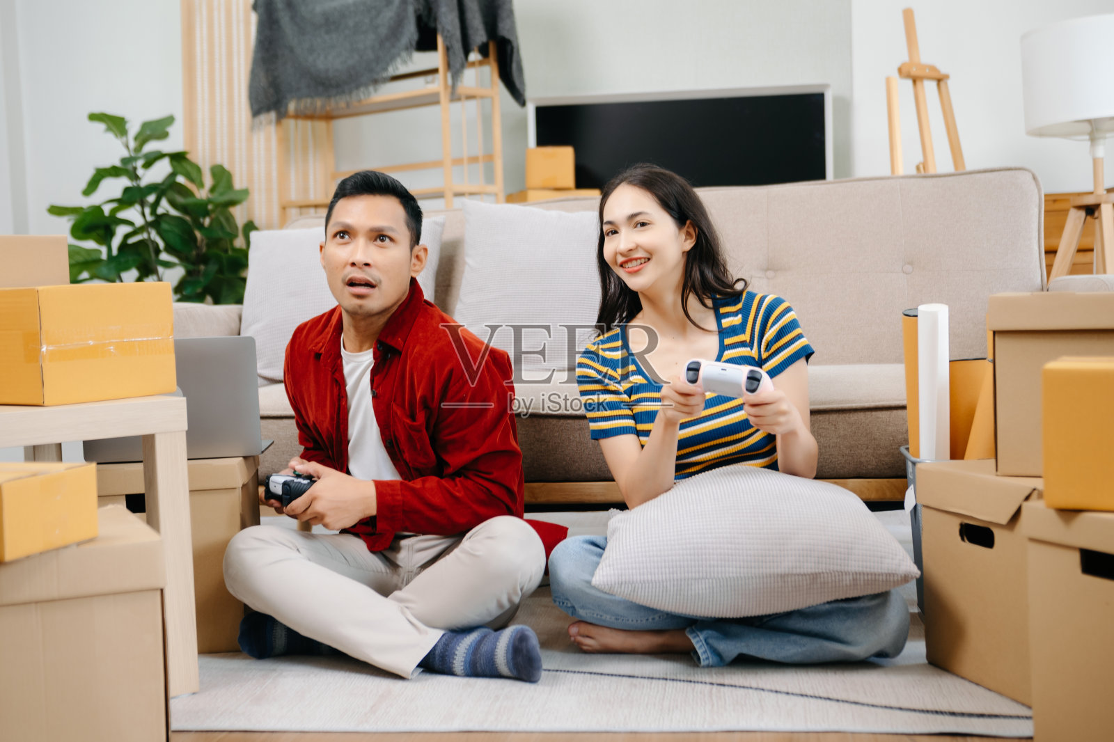 亚洲年轻夫妇男女坐在沙发上，用摇杆控制器玩电子游戏，一起在客厅的沙发上度过愉快的时光。亚洲已婚夫妇照片摄影图片