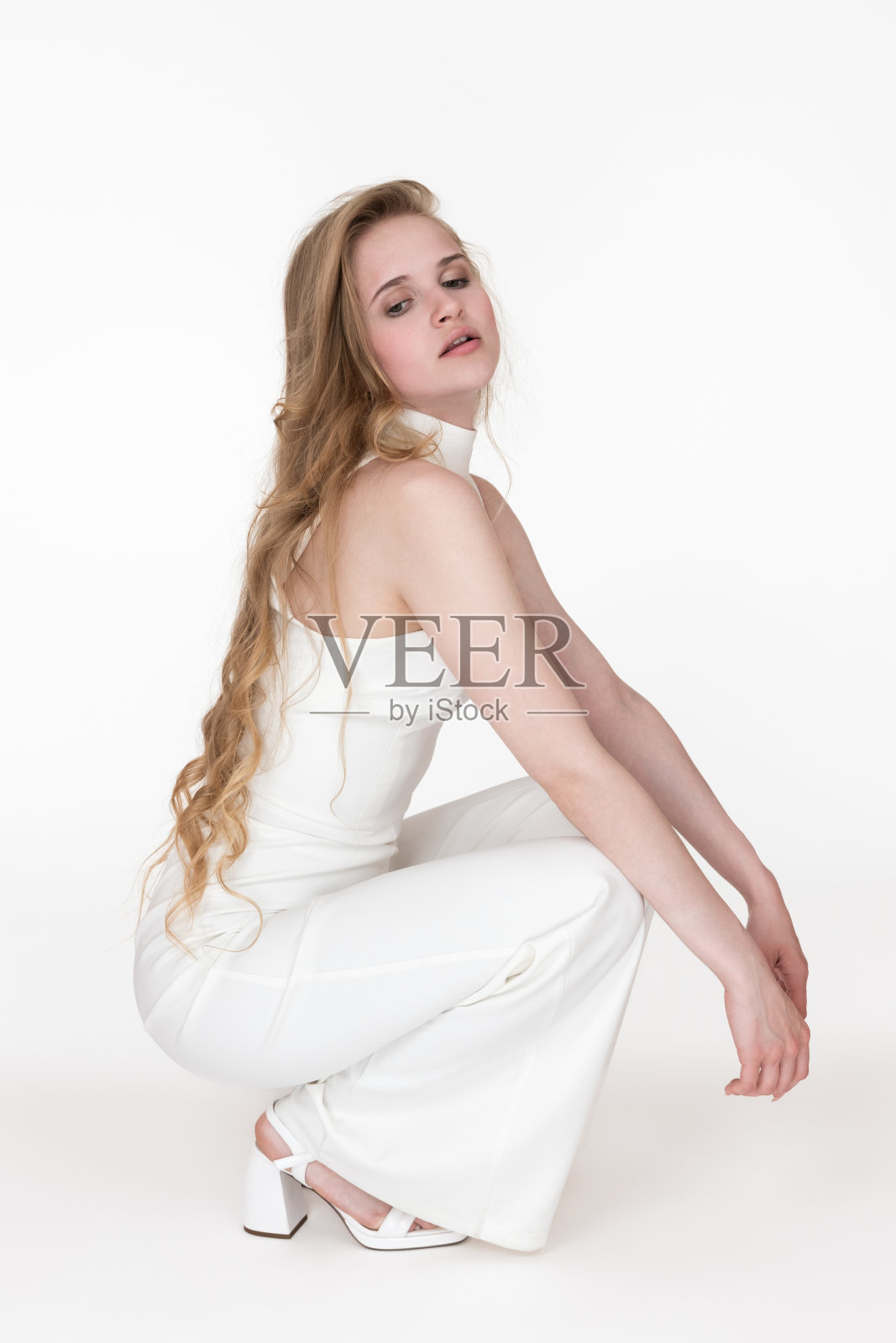 侧视图身穿白色连衣裤的女子蹲坐，双手放在膝盖上，向下看照片摄影图片