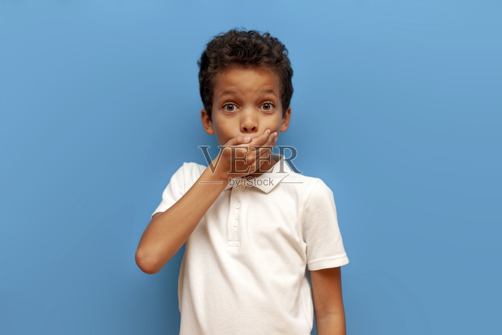 震惊的非洲裔美国少年很惊讶，用手捂住嘴在蓝色孤立的背景照片摄影图片