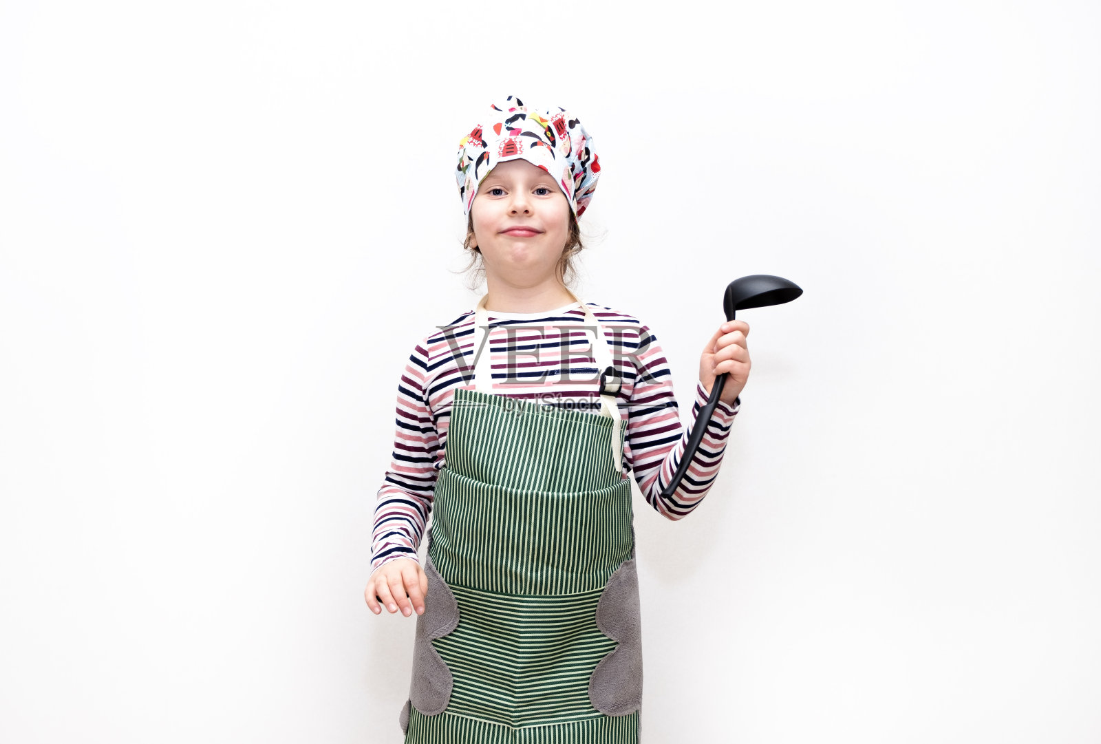 一个8岁的白人女孩，打扮成厨师，手里拿着勺子，微笑着。情感的脸。照片摄影图片