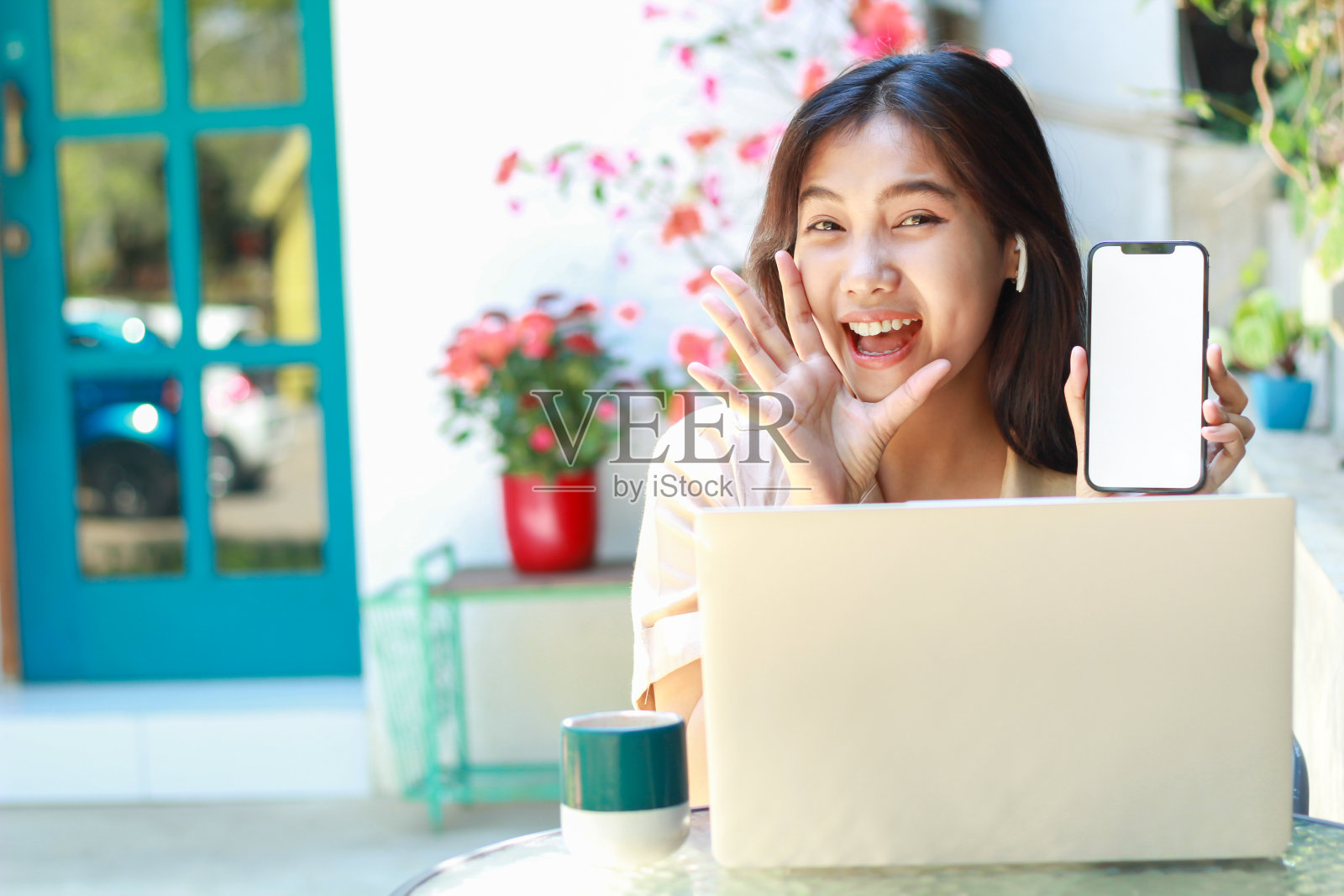 惊讶的亚洲女子坐在咖啡馆里，穿着休闲服，展示着智能手机屏幕，对着镜头大喊大叫照片摄影图片