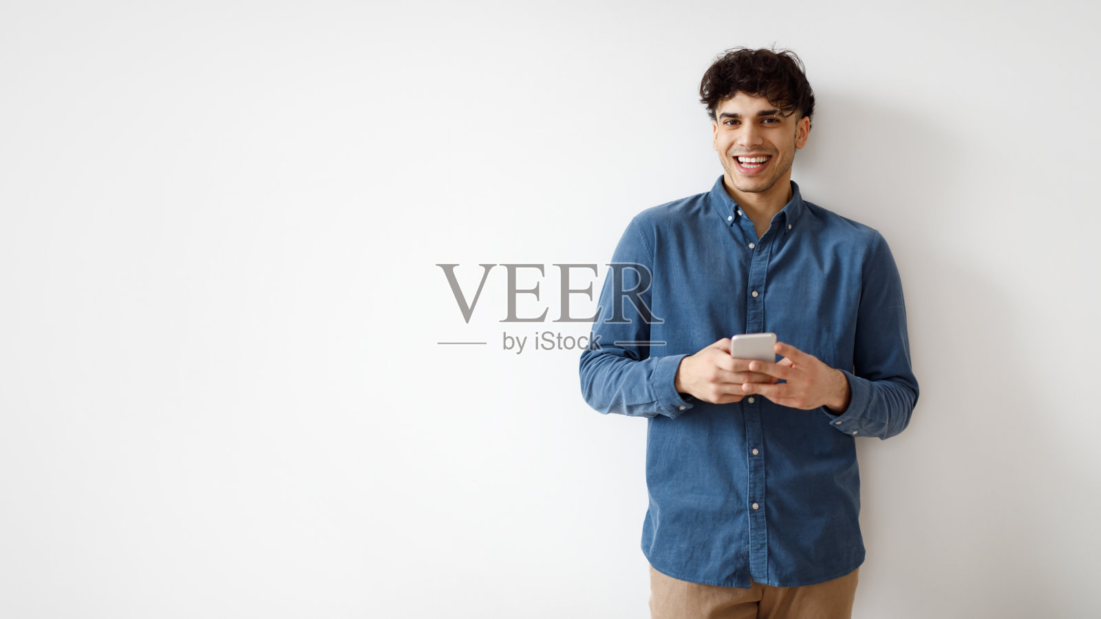 阿拉伯人在白墙附近用智能手机浏览社交媒体照片摄影图片