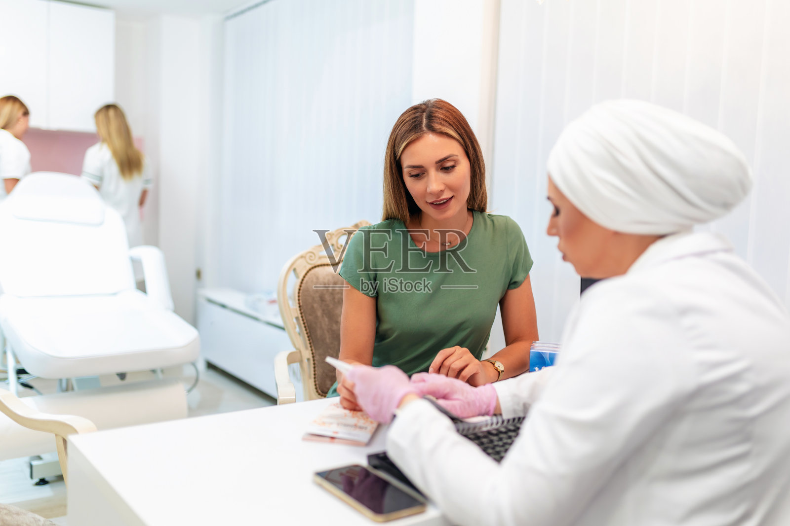 年轻漂亮的女人在美容院咨询美容师关于抗衰老治疗照片摄影图片