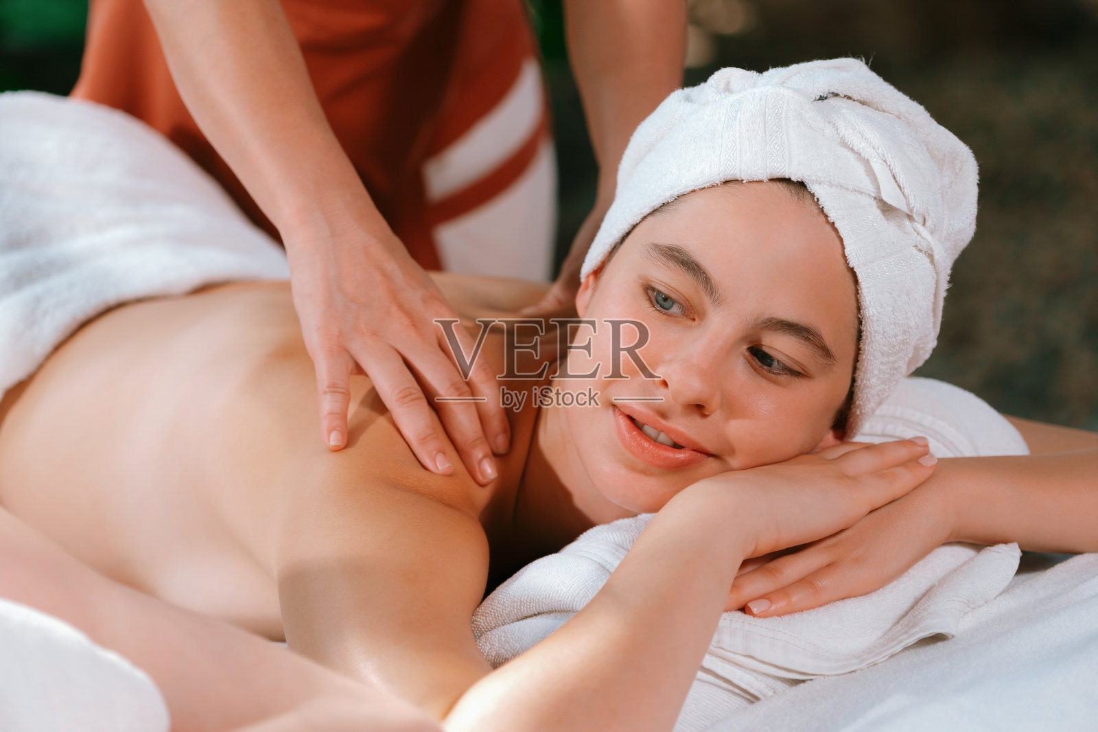 美丽的年轻女子在温泉床上接受背部按摩。宁静。照片摄影图片