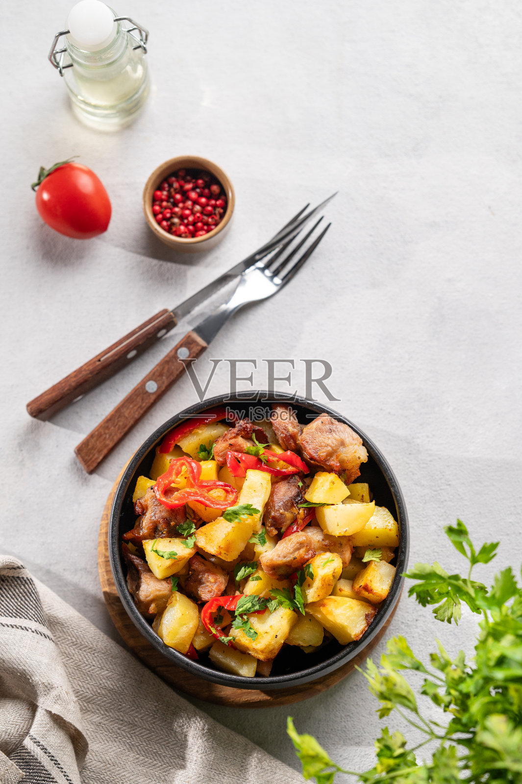 用土豆、洋葱和辣椒炒猪肉。格鲁吉亚国家自制菜肴ojakhuri在一个黑色的碗在浅背景新鲜的香草，香料和西红柿。照片摄影图片