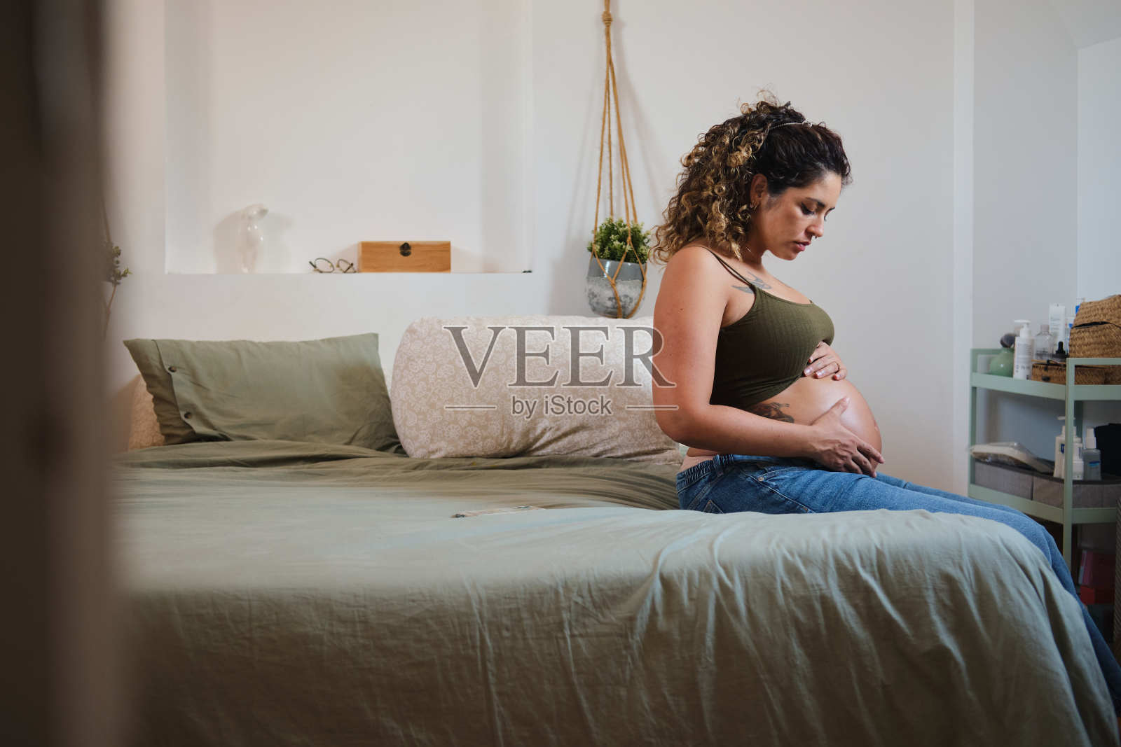 一个千禧一代自信的孕妇坐在床边抚摸并检查自己的肚子照片摄影图片