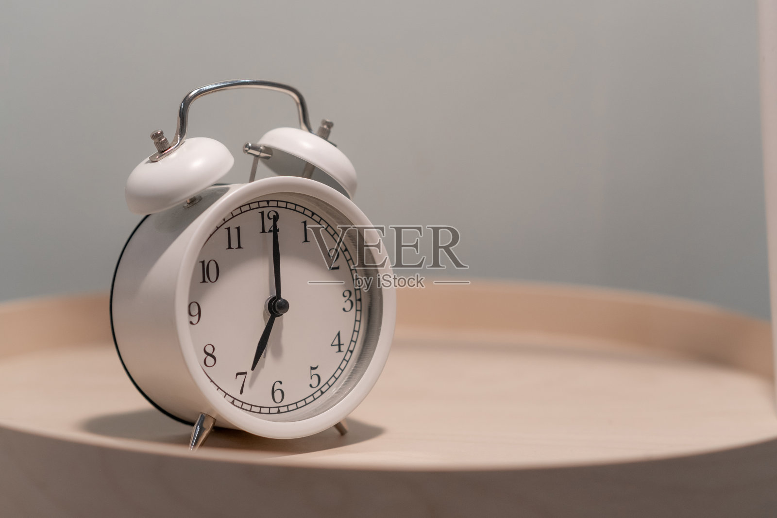 卧室桌子上一个白色圆形闹钟的特写。照片摄影图片