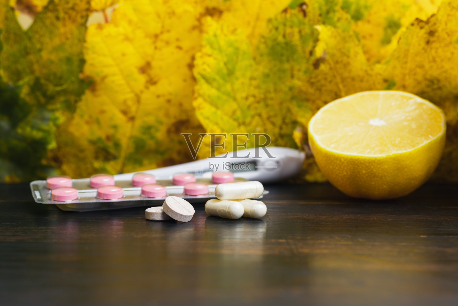 胶囊，药片，泡罩包装的药，温度计，放在黄叶子木桌上的柠檬。治疗秋季感冒、流感和冠状病毒的概念照片摄影图片
