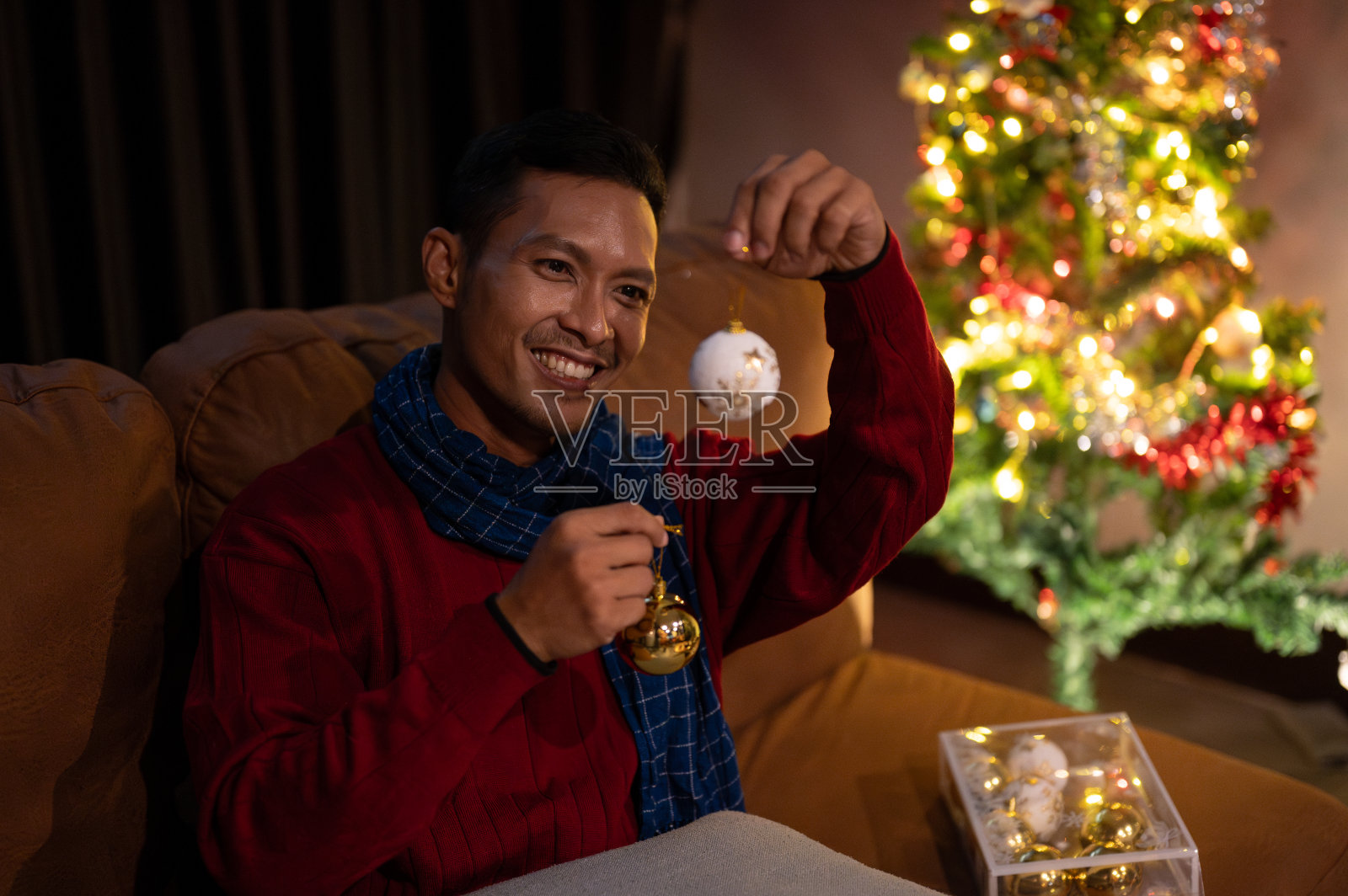 一个快乐的亚洲男人正在家里欣赏美丽的圣诞装饰品，庆祝他的圣诞节。照片摄影图片
