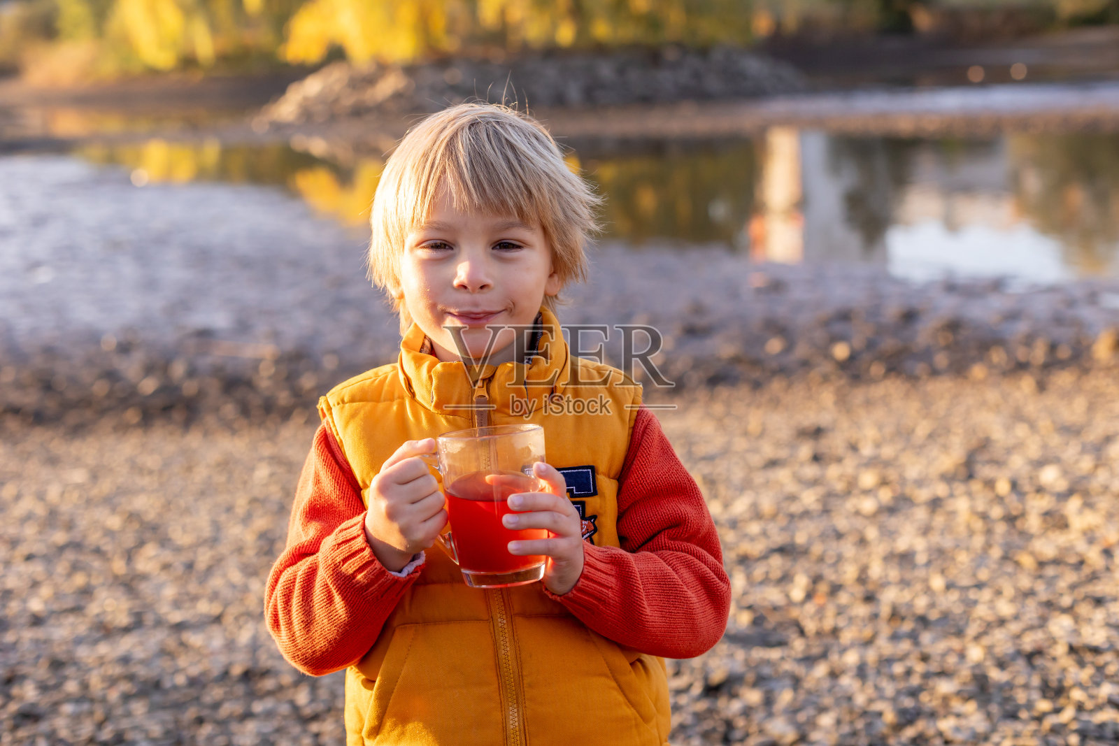 漂亮的金发学前班的孩子，男孩，坐在公园里，在清晨的日出，享受秋天的天气，喝着茶照片摄影图片