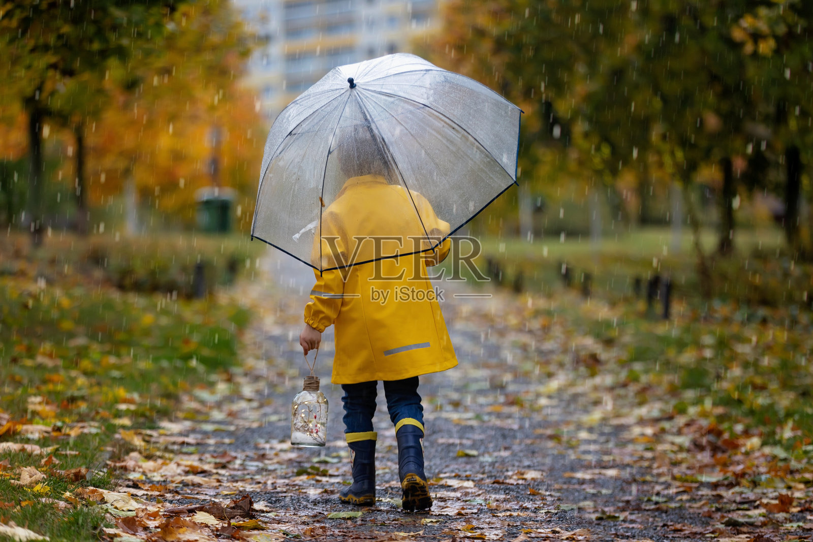 漂亮的金发学前班的孩子，打着伞在雨中玩树叶、蘑菇和南瓜照片摄影图片