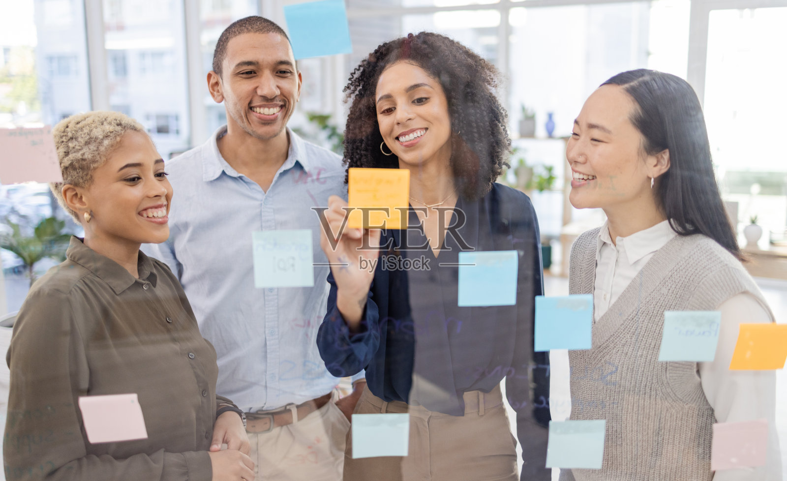 商务人士，在办公室的玻璃墙上撰写和安排战略计划或头脑风暴。快乐的设计师团队合作，微笑着为项目计划，任务或张贴它和便利贴照片摄影图片