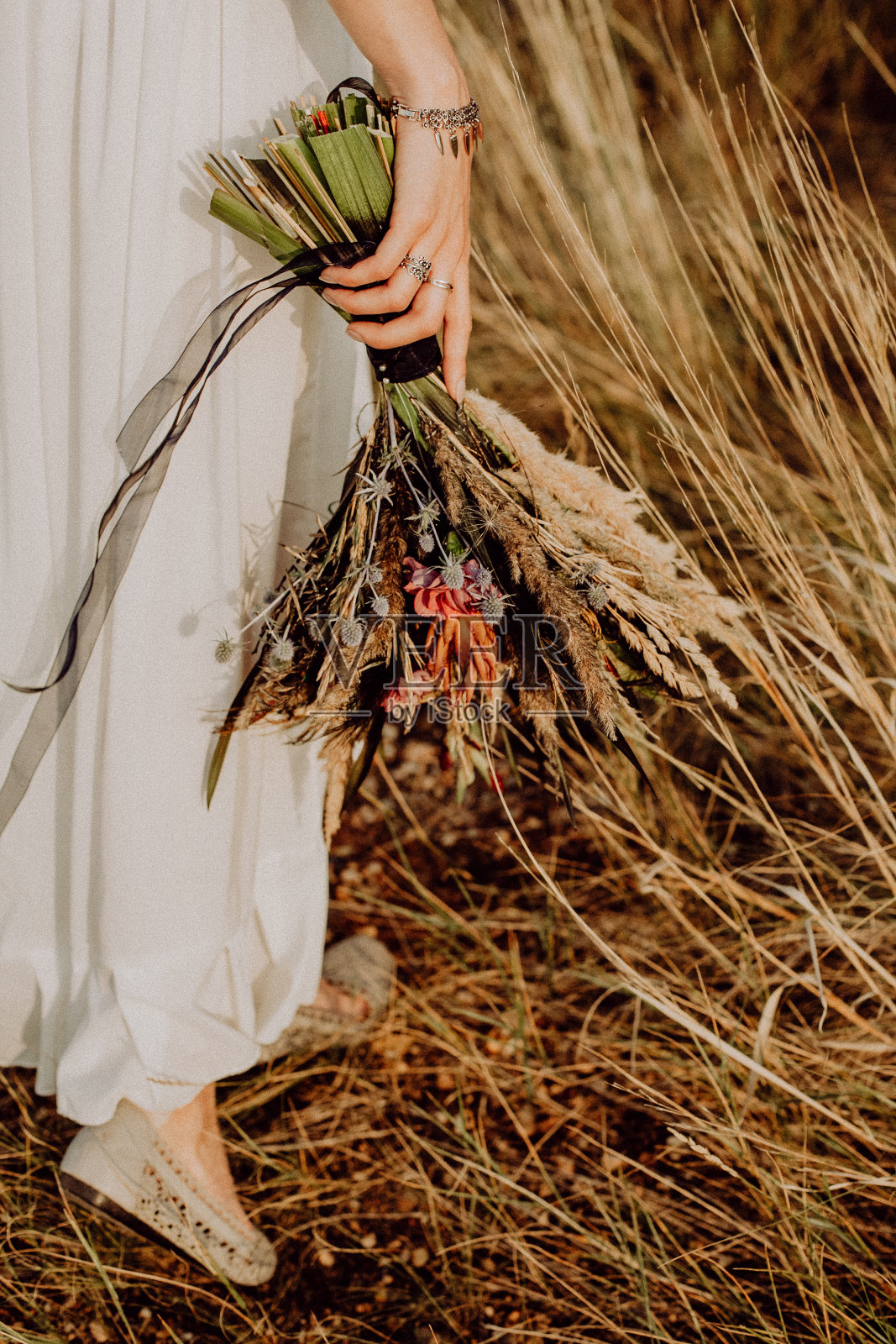 婚礼花束采自波西米亚风格的野花，新娘手里捧着花束，在大自然中，白色的礼服，活的植物，干花组成照片摄影图片