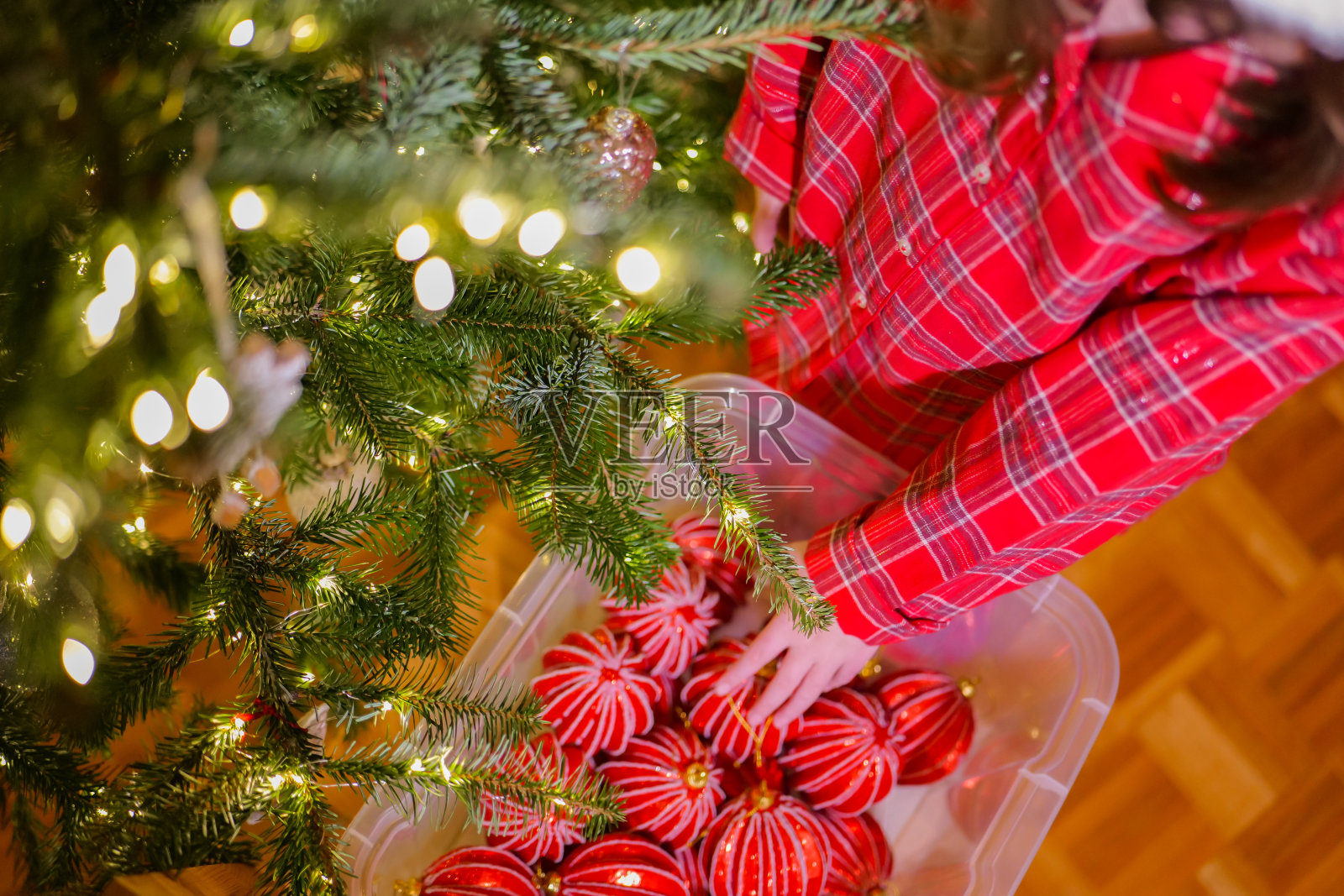 一个穿着红色格子睡衣的孩子手里拿着红色的球盒，旁边是一棵挂着花环的圣诞树。从上面看。圣诞树玩具。为寒假装饰一棵云杉树照片摄影图片