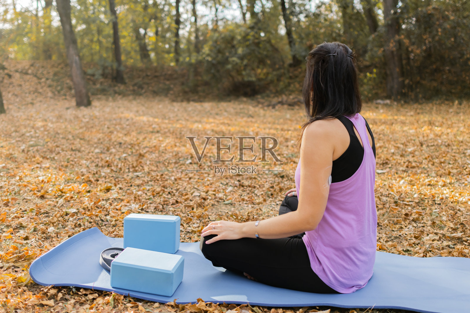 一位糖尿病患者在秋天的森林中练习瑜伽。她的上臂背部戴着一个控制血糖的小传感器。照片摄影图片