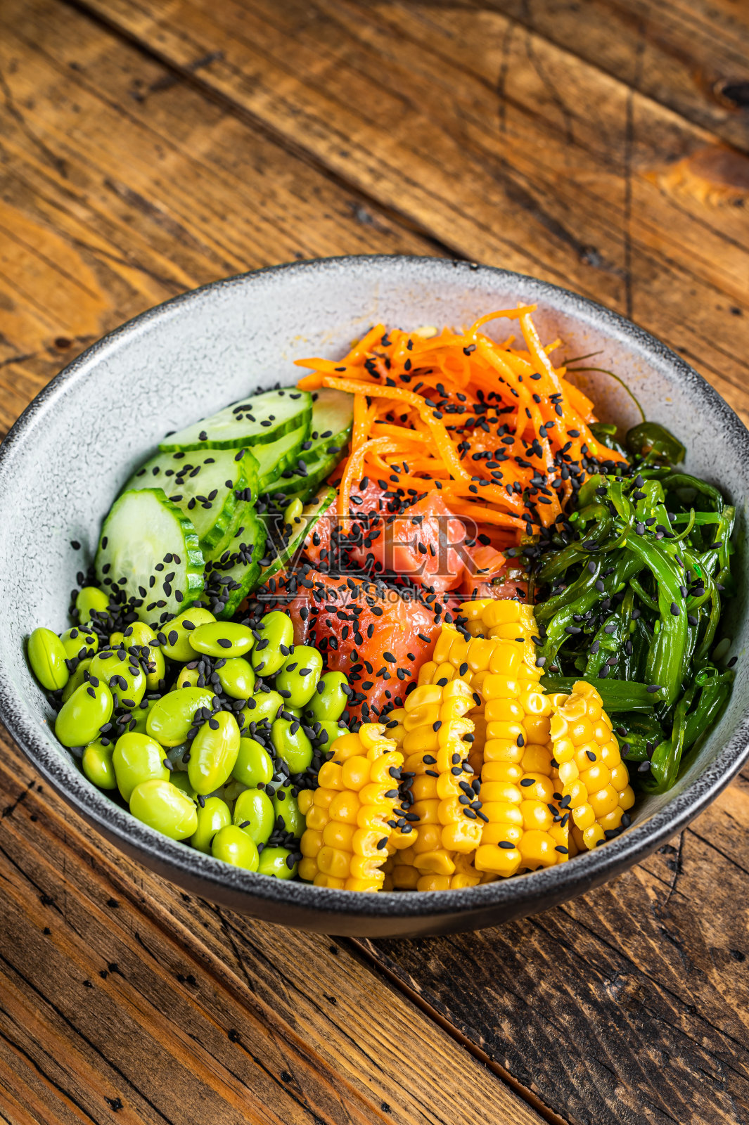 用新鲜的鲑鱼，米饭，海藻，毛豆，黄瓜和黑芝麻来泡碗。木制背景。俯视图照片摄影图片