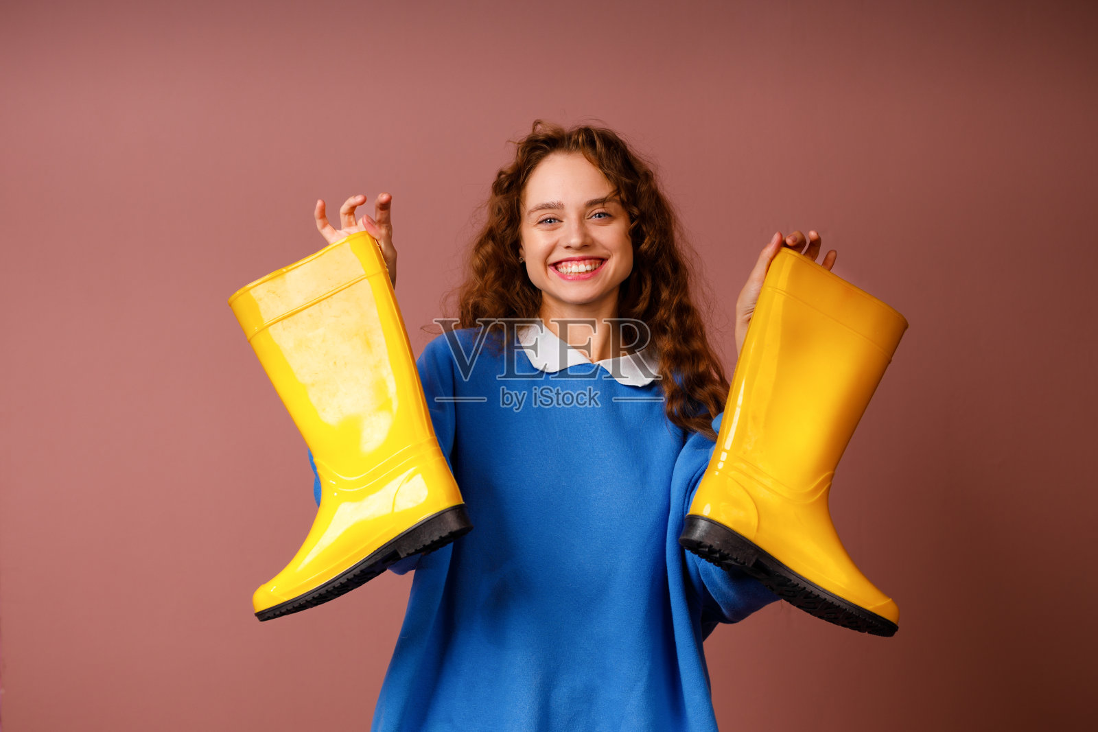 年轻、乐观、微笑的女人手里拿着一双胶靴。照片摄影图片