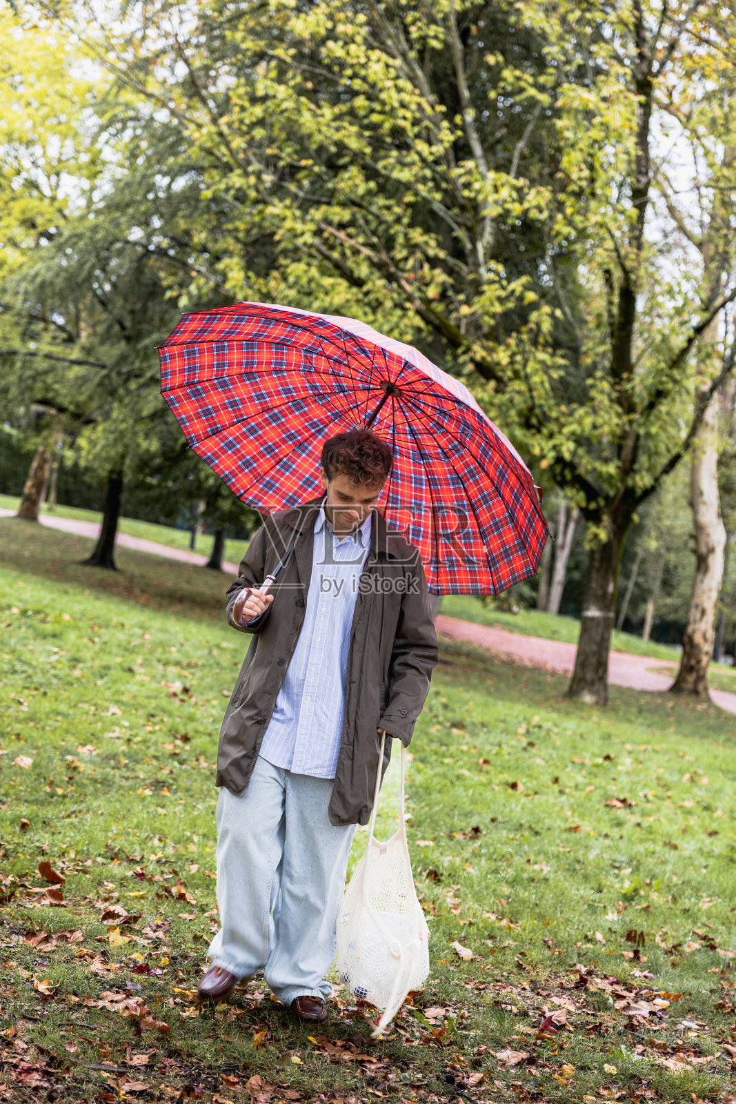 下雨天，一个年轻人在公园里打着伞收集塑料照片摄影图片