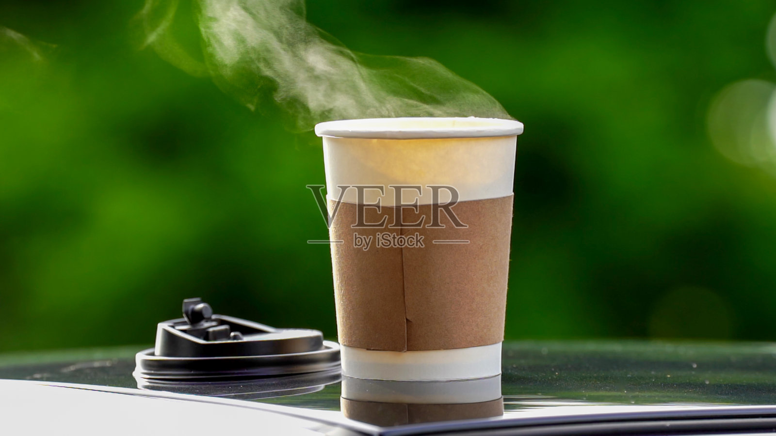 咖啡外卖在一个纸杯顶上的车顶绿树背景在日出的早晨，选择性聚焦，软聚焦。照片摄影图片