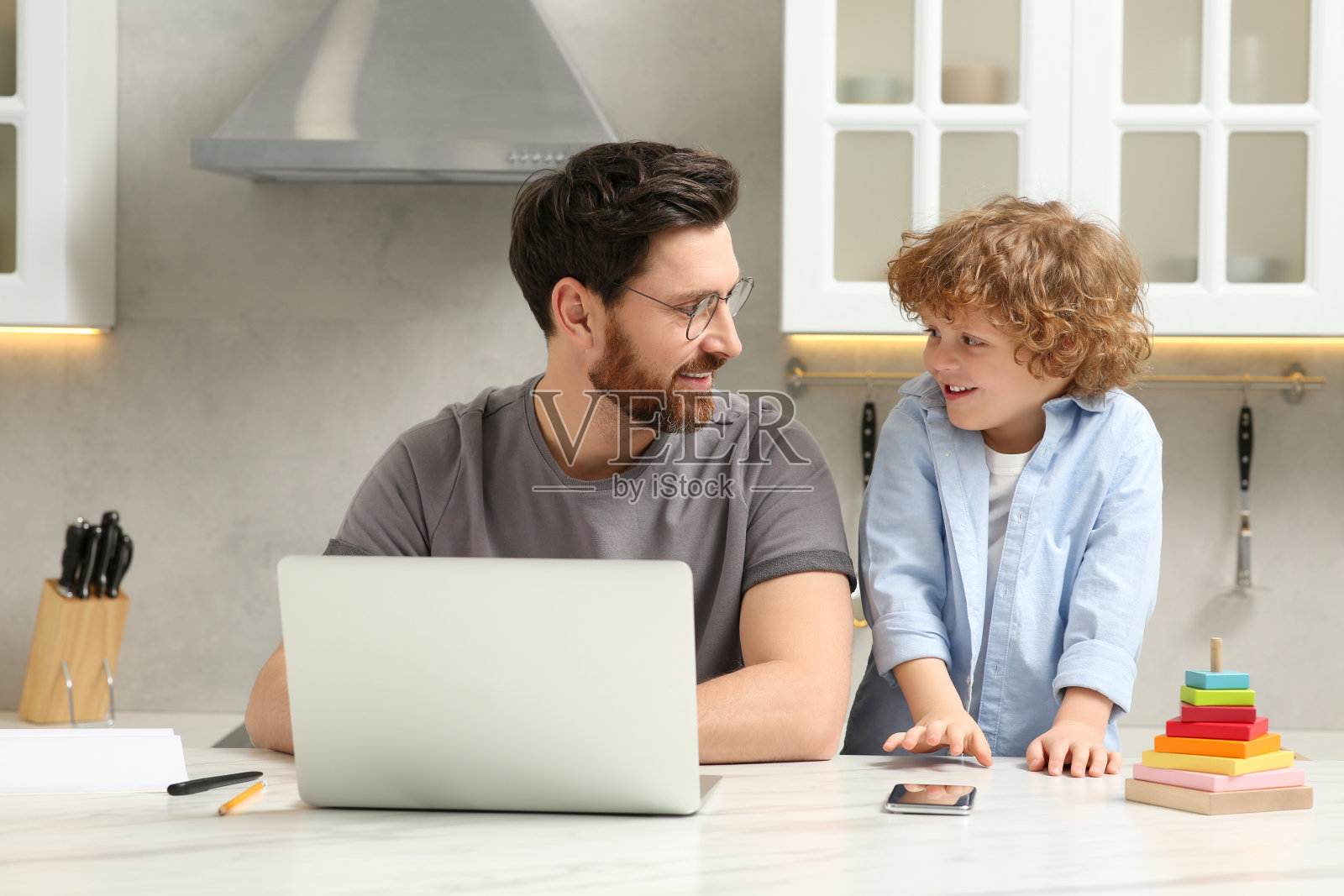 拿着笔记本电脑在家远程办公的人。父子坐在桌前照片摄影图片