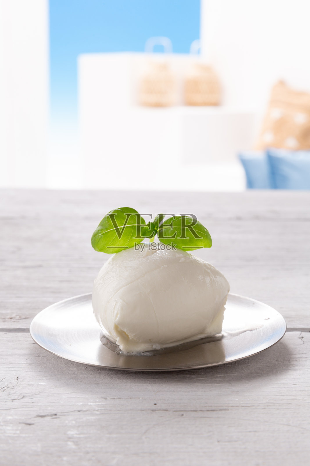 银色盘子里的马苏里拉奶酪和罗勒叶放在浅色木桌上，可以看到外面的景色照片摄影图片