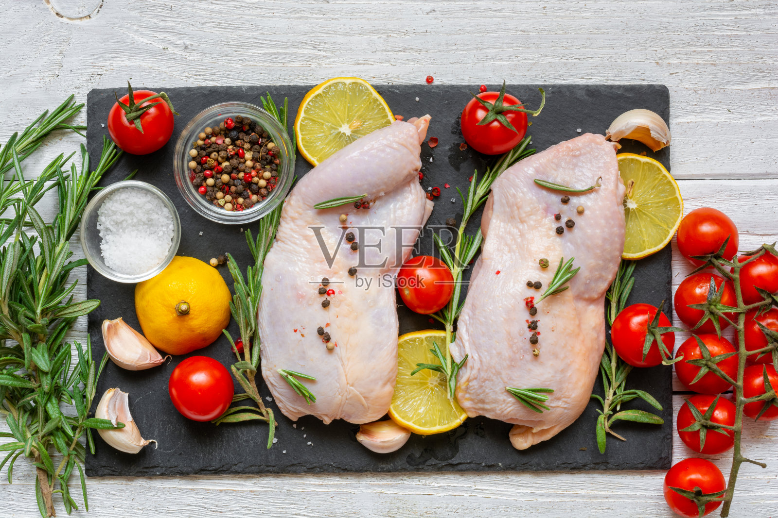 生鸡腿配番茄，樱桃，柠檬，大蒜，香料和香草，黑色石板，白色木制背景。前视图。煮肉做美味的晚餐。健康饮食食品照片摄影图片