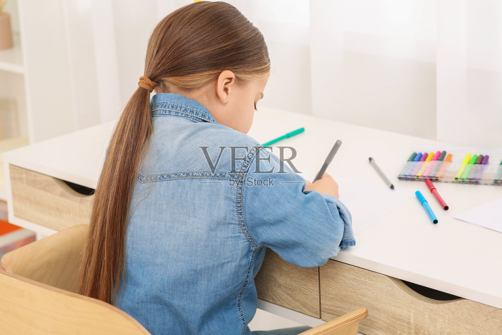 可爱的小女孩在房间的书桌上用马克笔画画。回家工作照片摄影图片