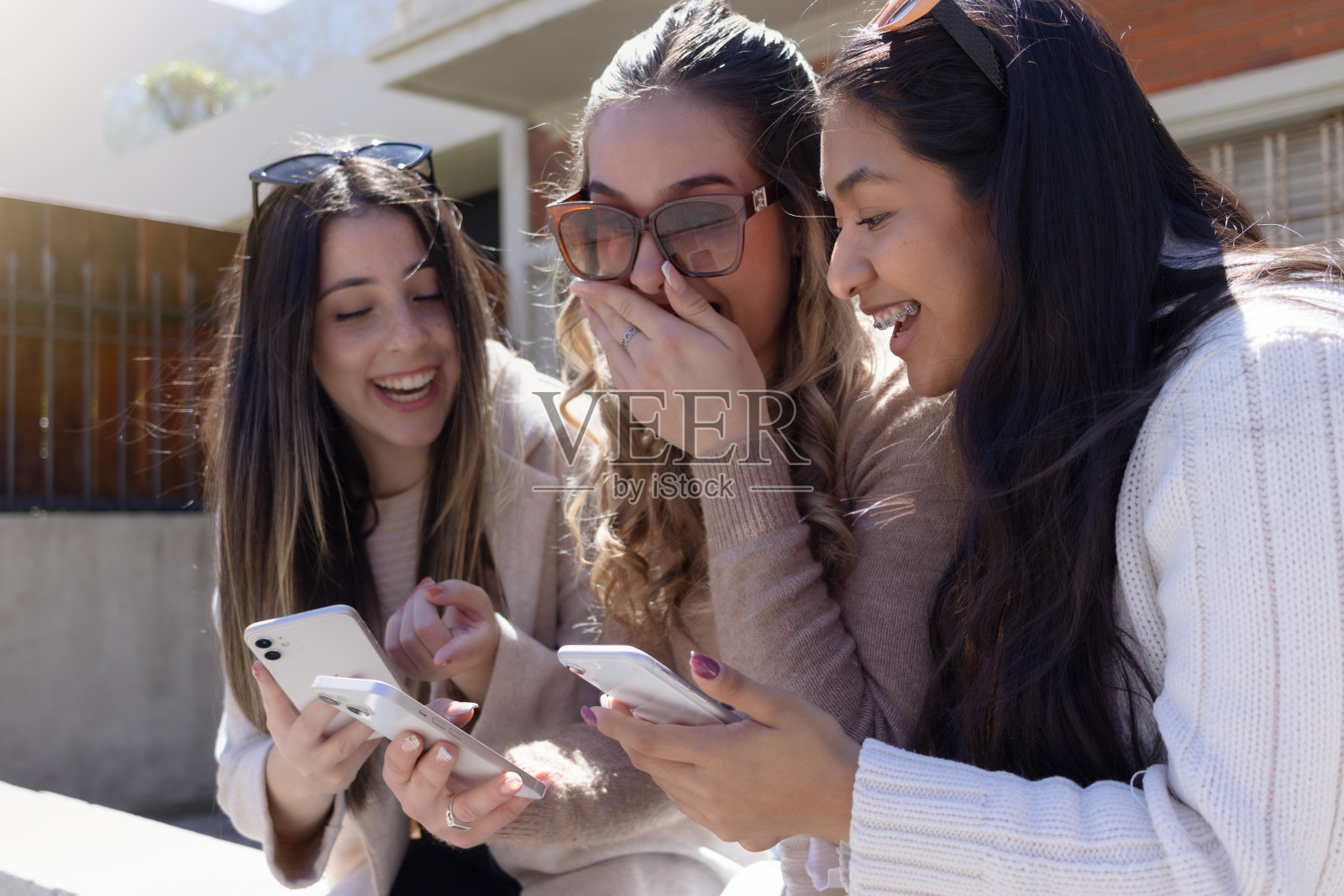 年轻的金发女郎和另外两个朋友在街上惊讶地看着她的智能手机。城市概念，青春，惊喜。照片摄影图片