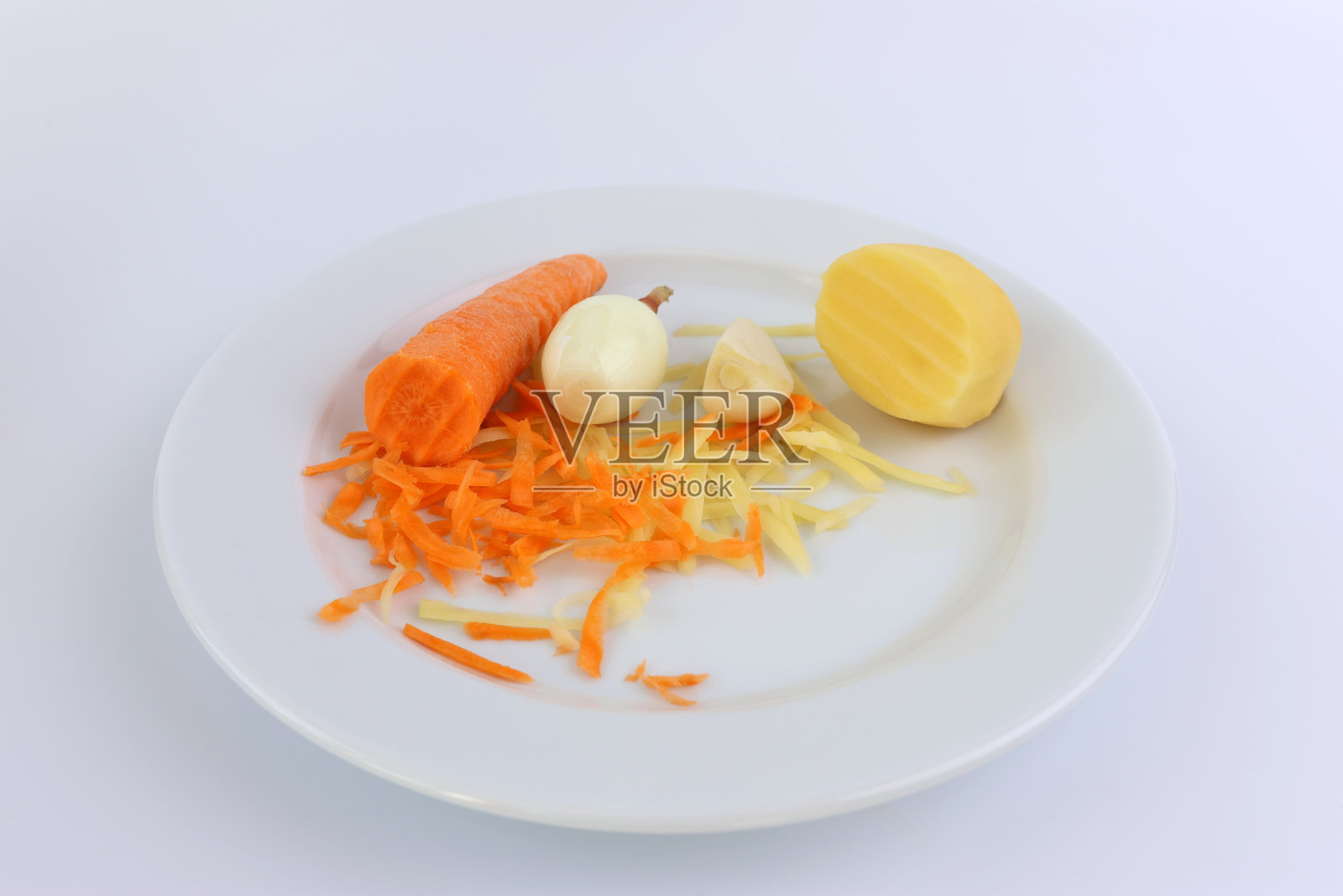 把蔬菜、土豆、胡萝卜、洋葱和大蒜磨碎放在一个白色盘子里。照片摄影图片