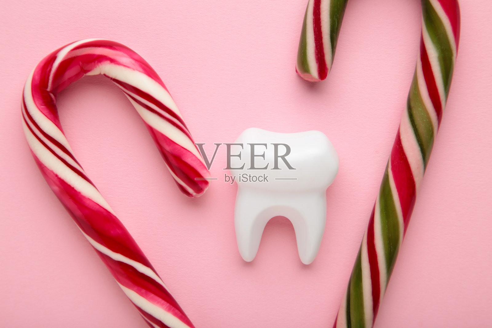 牙医。圣诞假期。牙齿小雕像与糖果在粉红色的背景。照片摄影图片