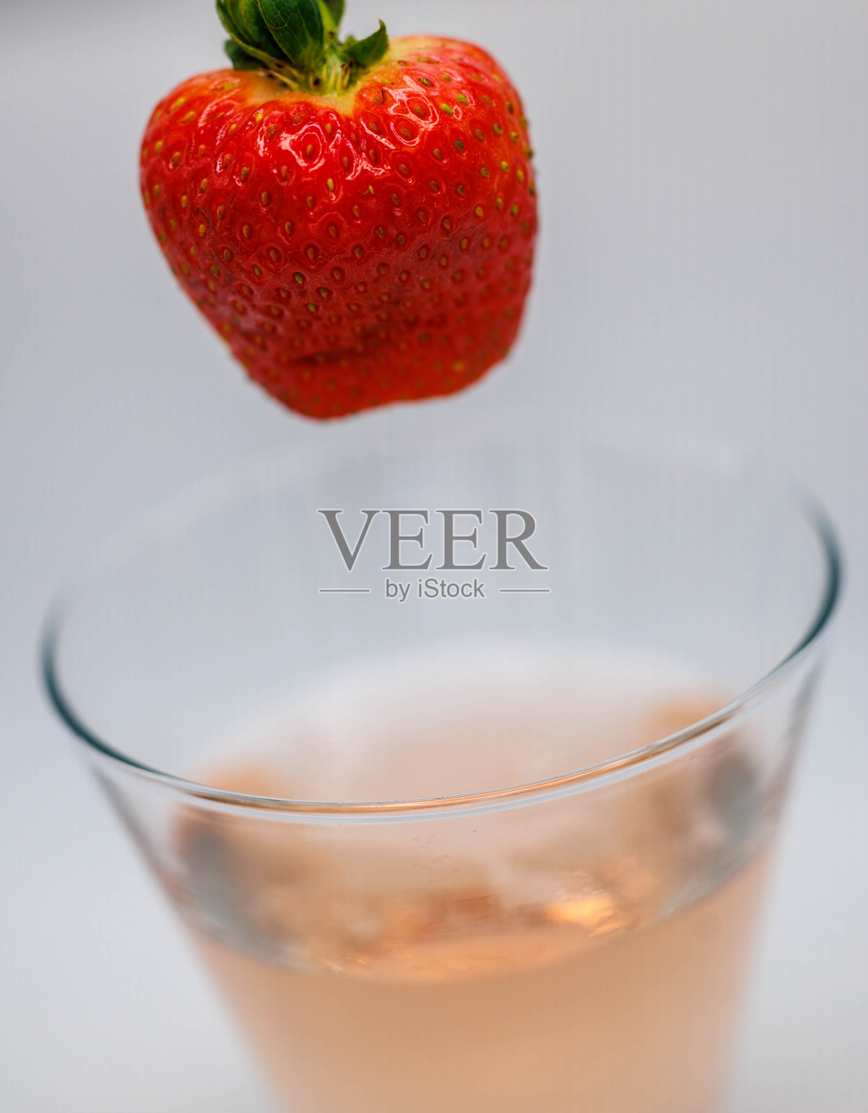 一个草莓和玫瑰鸡尾酒一起落入玻璃杯的特写照片照片摄影图片
