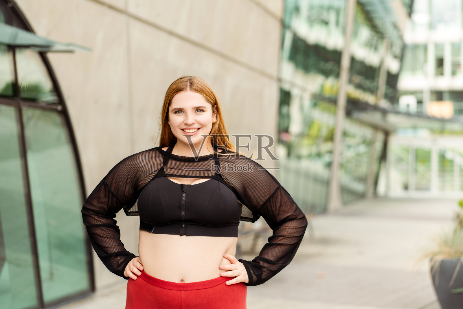 快乐的漂亮女人穿着运动上衣和打底裤，站在城市里。身体积极，体型大，有动力照片摄影图片