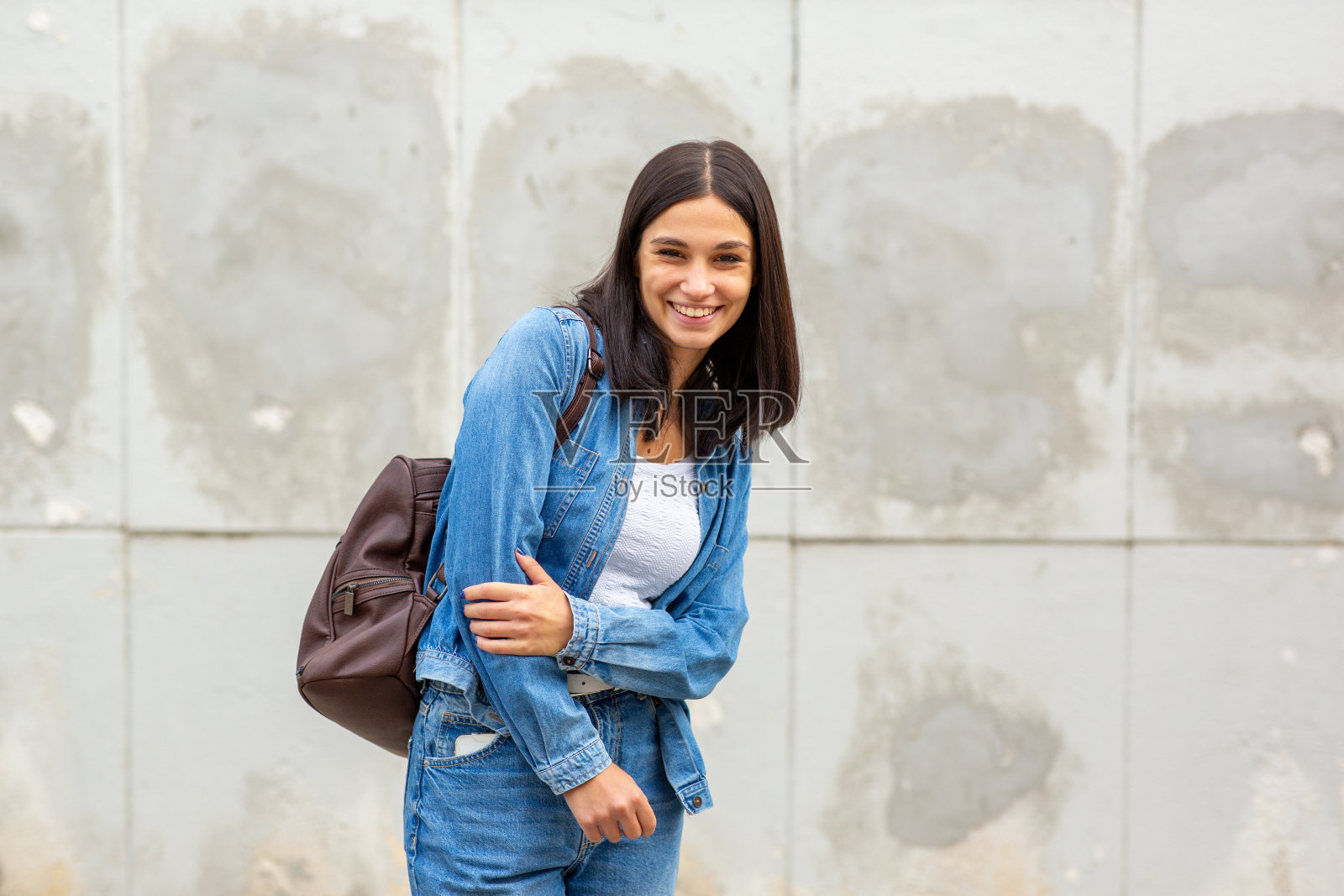年轻女子微笑着把包放在墙边照片摄影图片